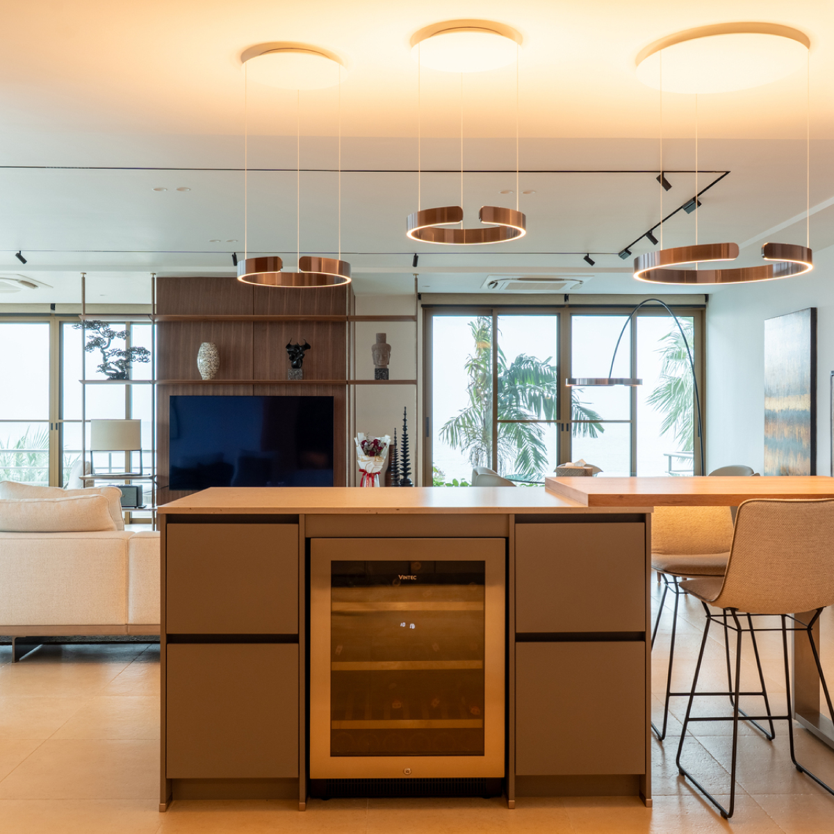 Modern kitchen island with a built-in wine fridge, pendant lights, and a view into a living area.