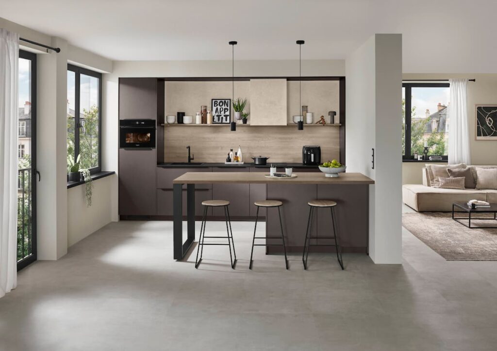 A minimalist kitchen design in a Bangkok condo featuring a rust red handleless island that acts as a furniture piece, seamlessly blending with the open-plan living area. 