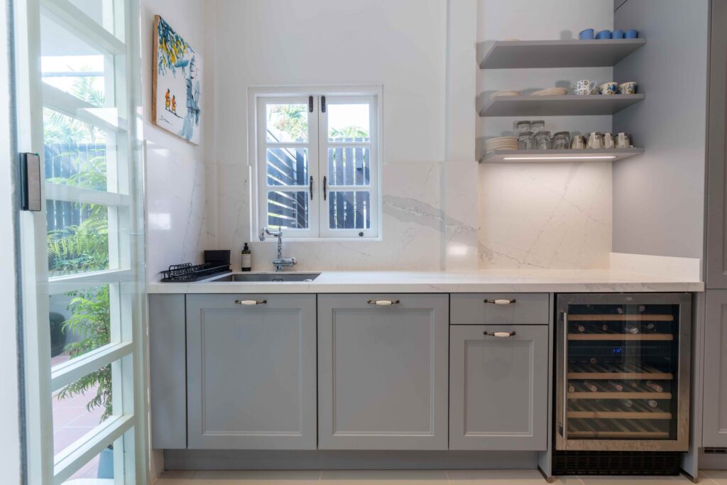 Bright sink area in a cottage kitchen featuring a seamless quartz backsplash and traditional window detail. 