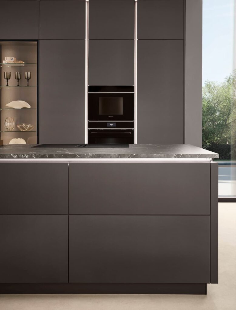 Close-up detail of a handleless modern kitchen showing the illuminated recessed LINE One design, ultra-matte dark cabinet fronts, and a slim marble-effect worktop.