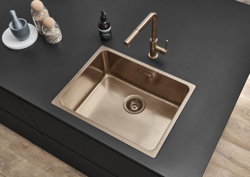 Modern kitchen design with a seamless bronze sink integrated into a matte black worktop, styled with spices and accessories.